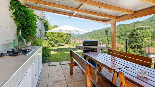 An outdoor kitchen area with a grill, a wooden table, and a bench. - Iris Holiday Home in Stellanello: Your Peaceful Retreat in Liguria (Rossi)