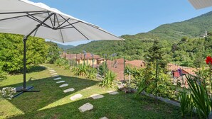 A garden with a patio umbrella, stone steps, and a view of houses in the background. - Iris Holiday Home in Stellanello: Your Peaceful Retreat in Liguria (Rossi)