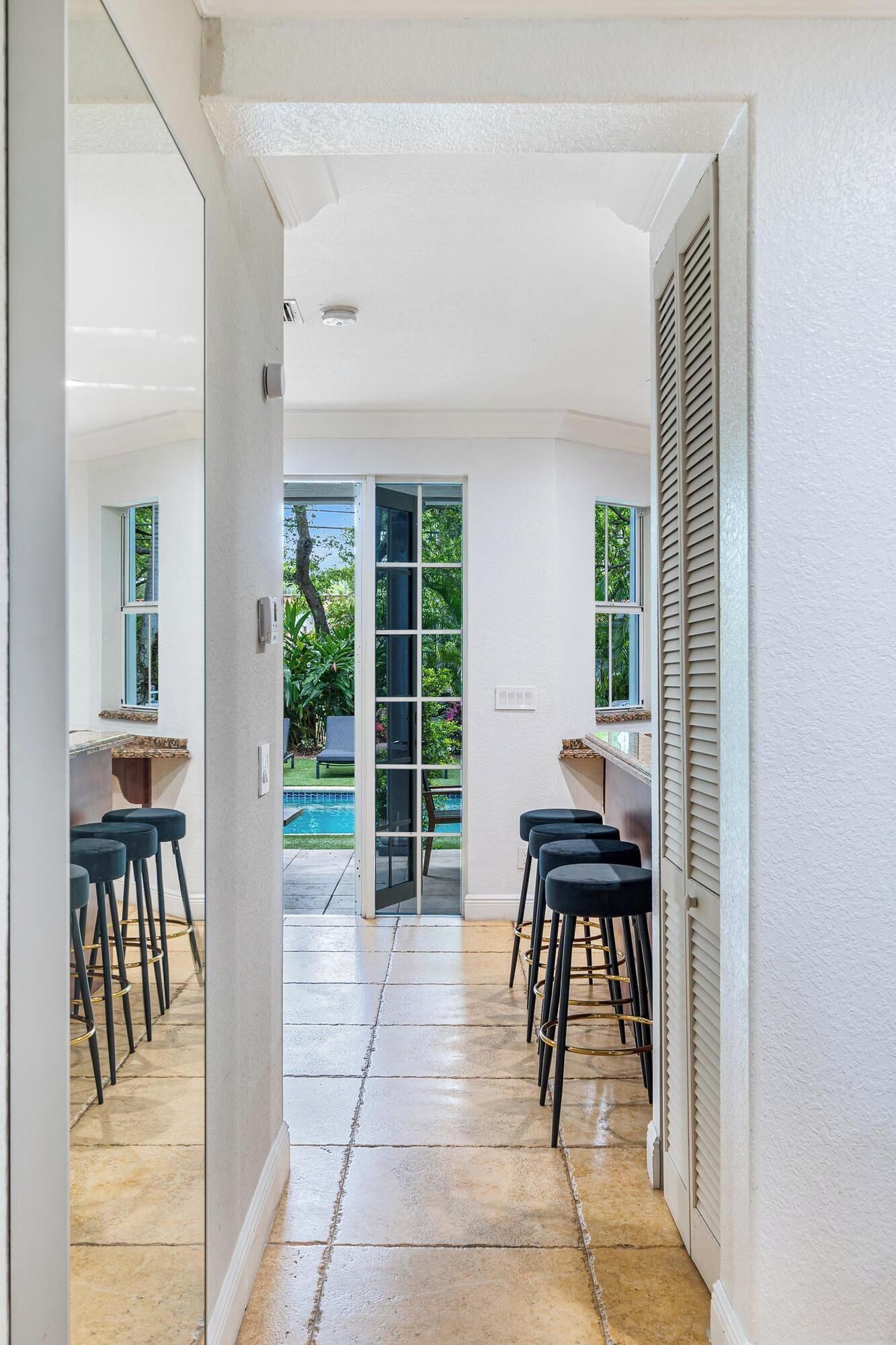 A modern interior with a kitchen area, a dining space with bar stools, and a view of a swimming pool.