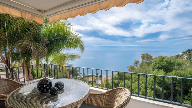 Un balcone con mobili in vimini, vista sul mare e vegetazione.