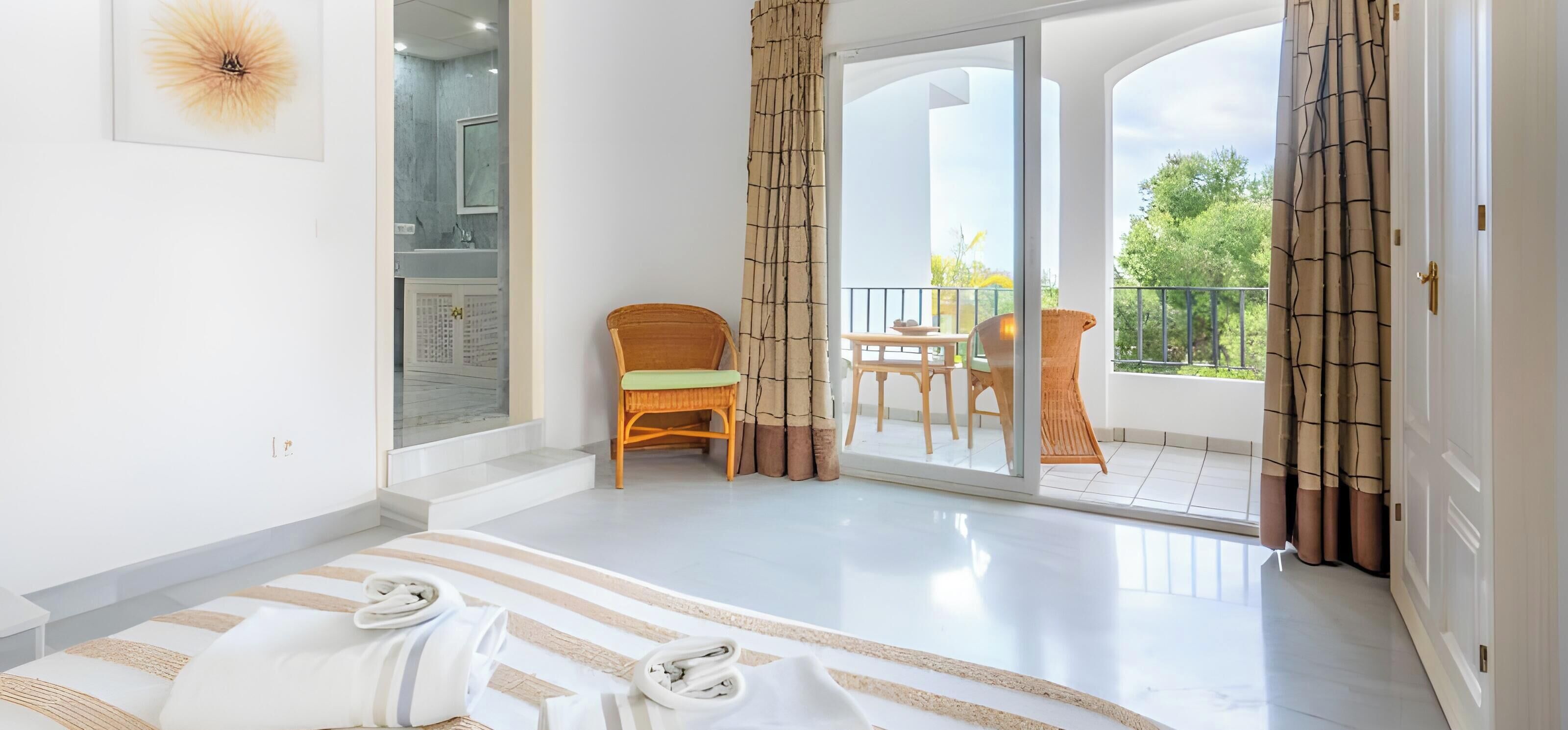 Una habitación de hotel con cama, una silla, una mesa y un balcón con cortinas.