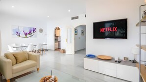 Un soggiorno moderno con divano, angolo da pranzo, cucina e TV che mostra il logo di Netflix.