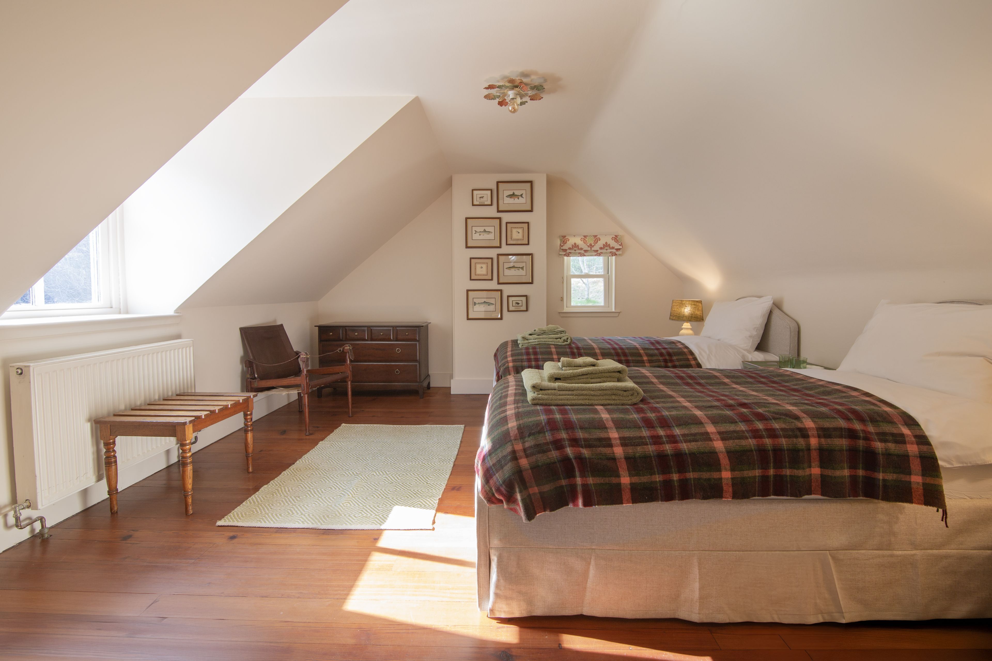 Een slaapkamer met een schuine plafond, een bed met een geruite deken, een stoel, een bureau en een radiator.
