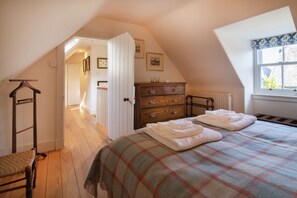 A bedroom with a sloped ceiling, a bed with a plaid blanket, a wooden dresser, and a window with a view. - Smithy Cottage -  Beauly , Scottish Highlands, Scotland (Beauly)