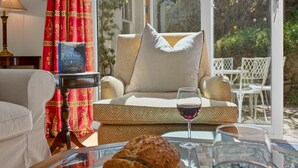 Una sala acogedora con un sofá, una mesa de vidrio, un libro y una copa de vino tinto.