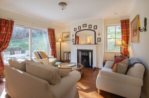 A living room with a fireplace, two sofas, a coffee table, and a view of the garden. - Smithy Cottage -  Beauly , Scottish Highlands, Scotland (Beauly)