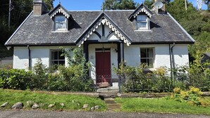 Una casa de dos pisos con puerta roja, paredes blancas y techo negro.
