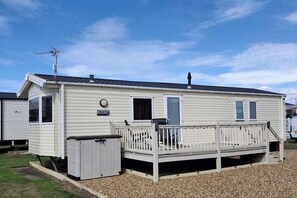 A mobile home with a fenced porch, a small attached garage, and a satellite dish. - 3 Bedroom Caravan Heacham by Amenities (King's Lynn)