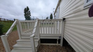 Um deck de madeira branca com corrimão, degraus que levam a uma casa e uma pequena caixa de plantas.