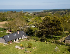 A house with a sloped roof, surrounded by a grassy yard and trees. - SPACIOUS COTTAGE BETWEEN LAND AND SEA - Sleeps 9, 5 bedrooms, 2 shower rooms, 3 toilets, ping-pong table (Veulettes-sur-Mer)