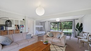 A modern living room with a sofa, a coffee table, a bunk bed, and a large window with a view of greenery. - Goldilocks in Teddy Bear Lane (Cowes)