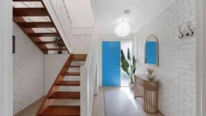A staircase with wooden steps and white walls, a blue door, a hanging light fixture, and a small potted plant. - Goldilocks in Teddy Bear Lane (Cowes)