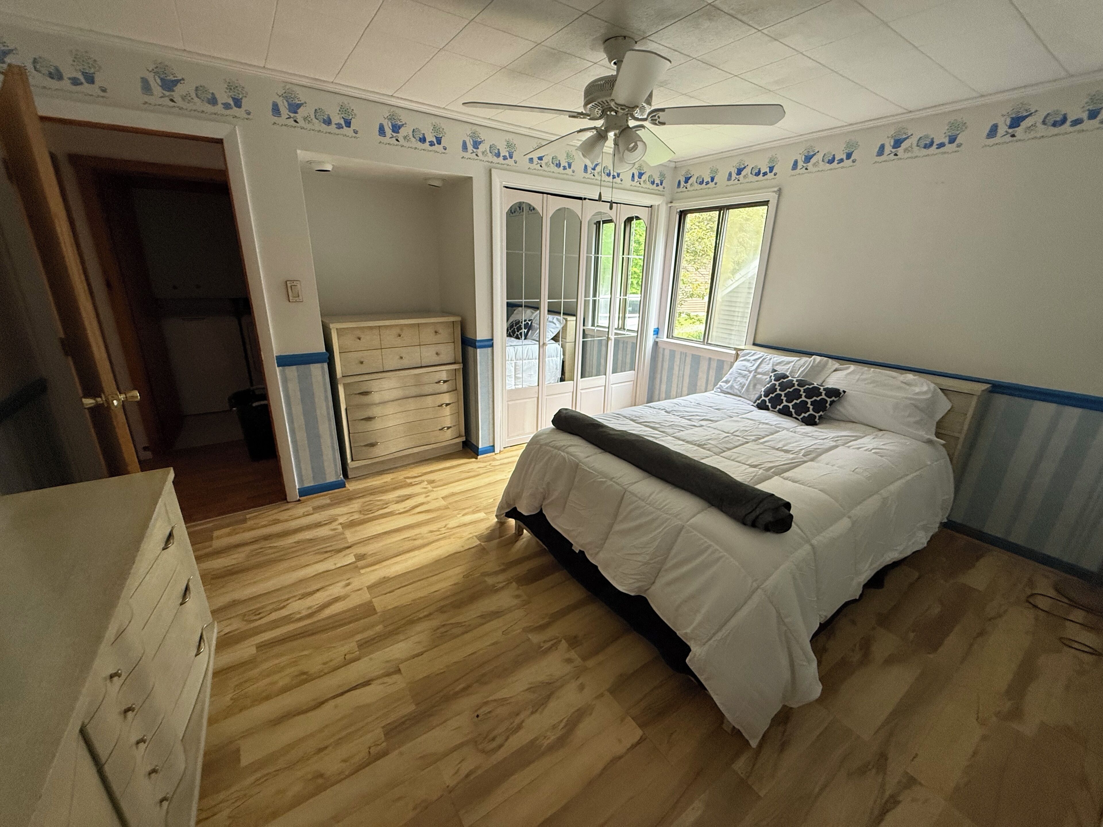 Una camera da letto con un letto, una cassettiera, una ventola a soffitto e una finestra.
