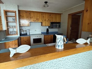 Uma cozinha com armários de madeira, micro-ondas, fogão e saleiro e pimenteiro em formato de peixe.