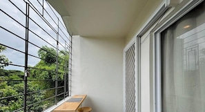 A balcony with a view of greenery, a window with a metal grid, and a wooden bench. - Cozy Pet-friendly Studio Condo in Cagayan de Oro (Cagayan de Oro)