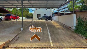 Uma área de estacionamento coberta com carros e uma motocicleta, um edifício ao fundo e uma placa com a inscrição 'parky's place'.