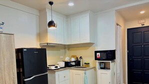 Uma cozinha compacta com armários brancos, uma geladeira preta, micro-ondas e uma luminária pendente.