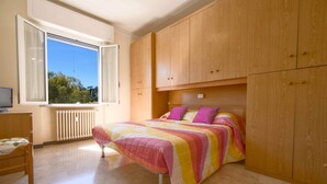 Ein Schlafzimmer mit Bett, Holzschrank, Fenster und Heizkörper.