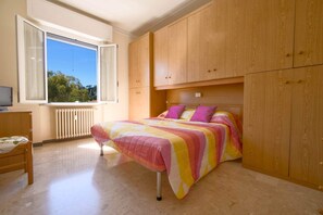 Ein Schlafzimmer mit Bett, Holzschrank, Fenster und Heizkörper.