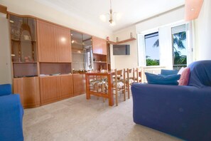 A living area with a dining table, chairs, a sofa, and a kitchen with cabinets and a TV. - Magirina House (Chiavari)