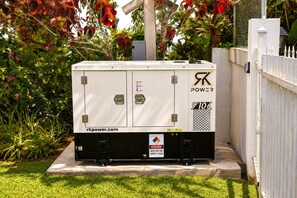 A portable power station with a warning label, placed outdoors on a concrete platform. - New Mountain Escape Panoramic San Juan Views (Aguas Buenas)