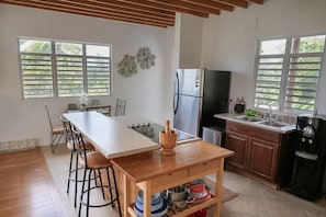A kitchen with a wooden table, bar stools, a refrigerator, a sink, and a coffee machine. - New Mountain Escape Panoramic San Juan Views (Aguas Buenas)
