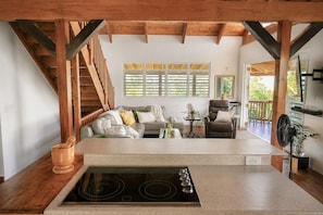 A modern kitchen with a built-in stove, wooden beams, a staircase, a sofa, and a dining area. - New Mountain Escape Panoramic San Juan Views (Aguas Buenas)