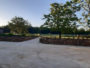 A paved driveway leading to a stone wall, surrounded by trees and a grassy area.