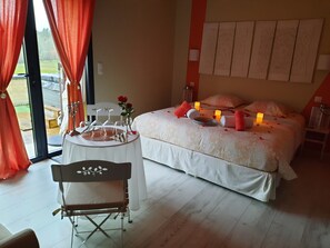 A bedroom with a bed, a bedside table with candles, a chair, and a view of the outdoors.
