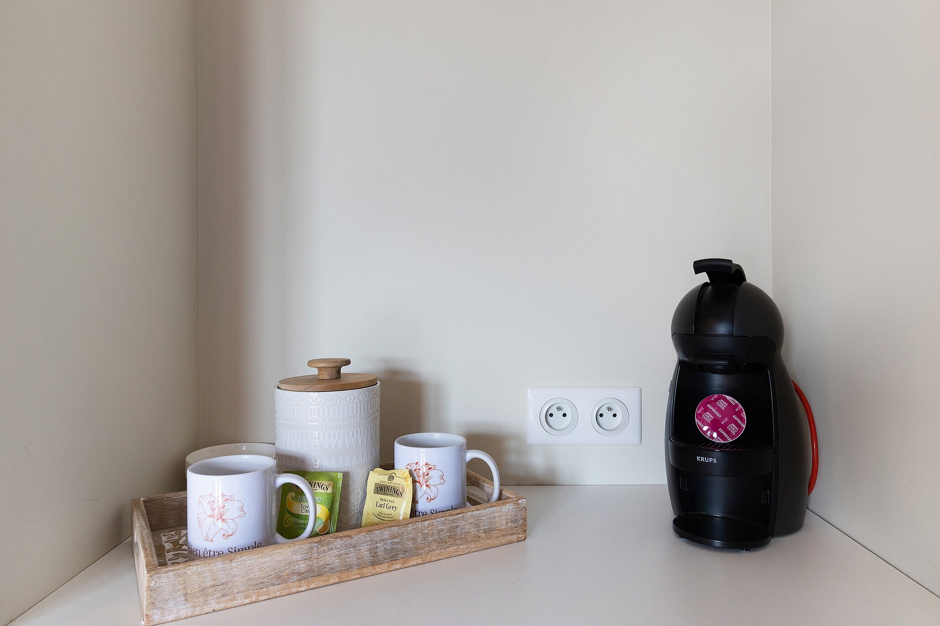 A kitchen counter with a coffee maker, a tray with mugs and a roll of paper towels, and a power outlet.