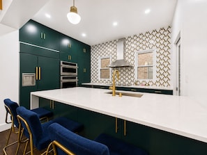 Une cuisine moderne avec des meubles de couleur vert foncé, un plan de travail blanc et un pare-feu décoratif.