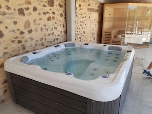 Een hottub met een achtergrond van een stenen muur, houten vloeren en een glazen scheiding.