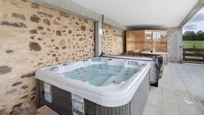 Un jacuzzi con un muro de piedra de fondo, una mesa de madera y vistas al exterior.