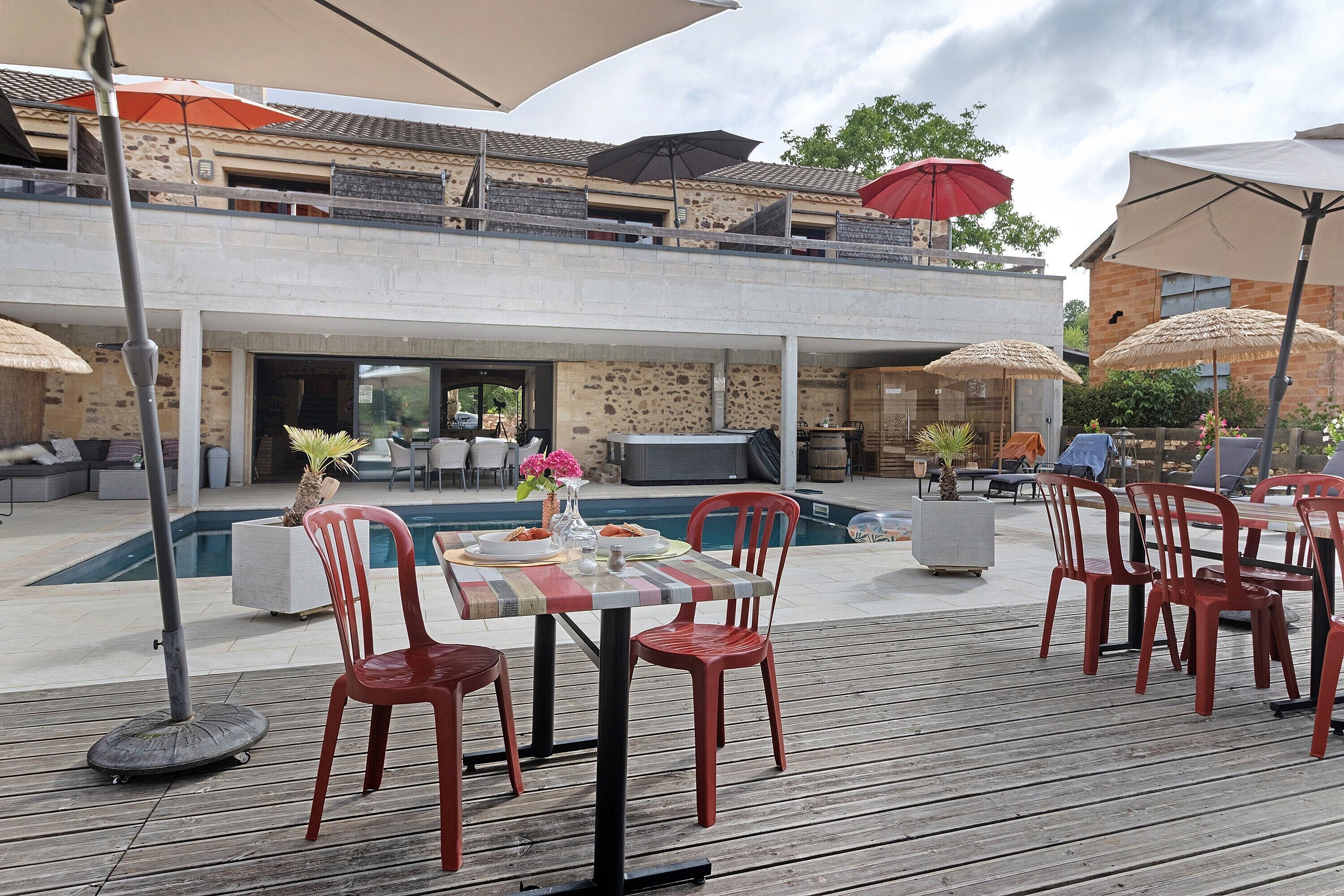 Un espace extérieur aménagé pour les repas, avec une piscine, des chaises rouges et des parasols.