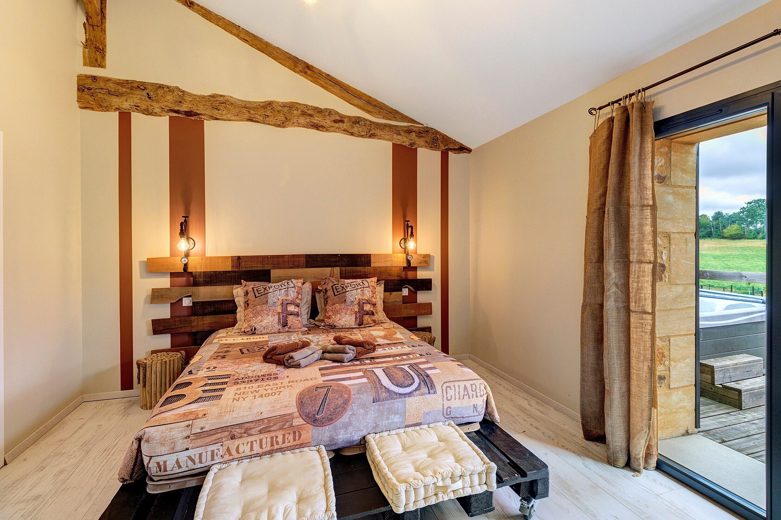 Een slaapkamer met een groot bed, houten balken, uitzicht op de omgeving en een stenen muur.