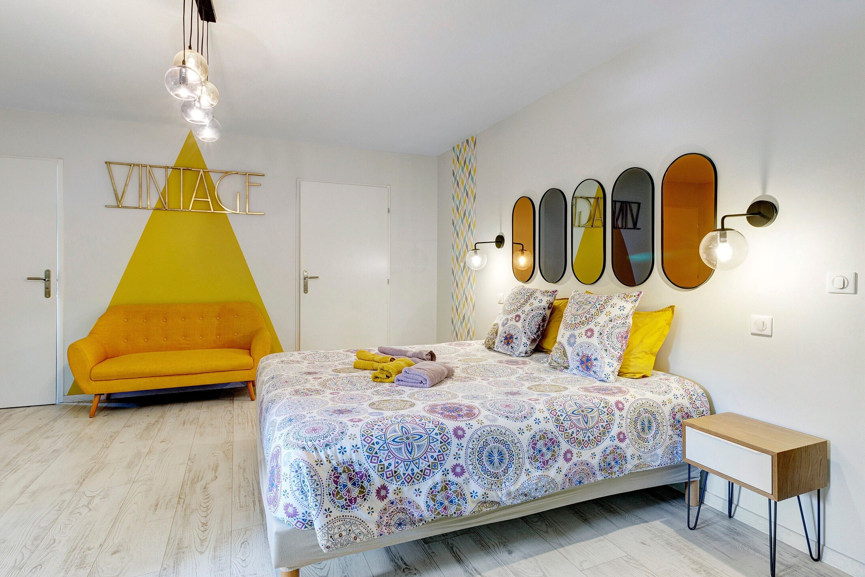 Een slaapkamer met een bed, een sofa, een nachtkastje en een wand met decoratieve spiegels.