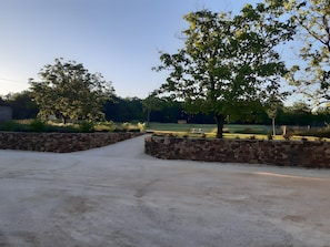 A paved driveway leading to a stone wall, surrounded by trees and a grassy area.
