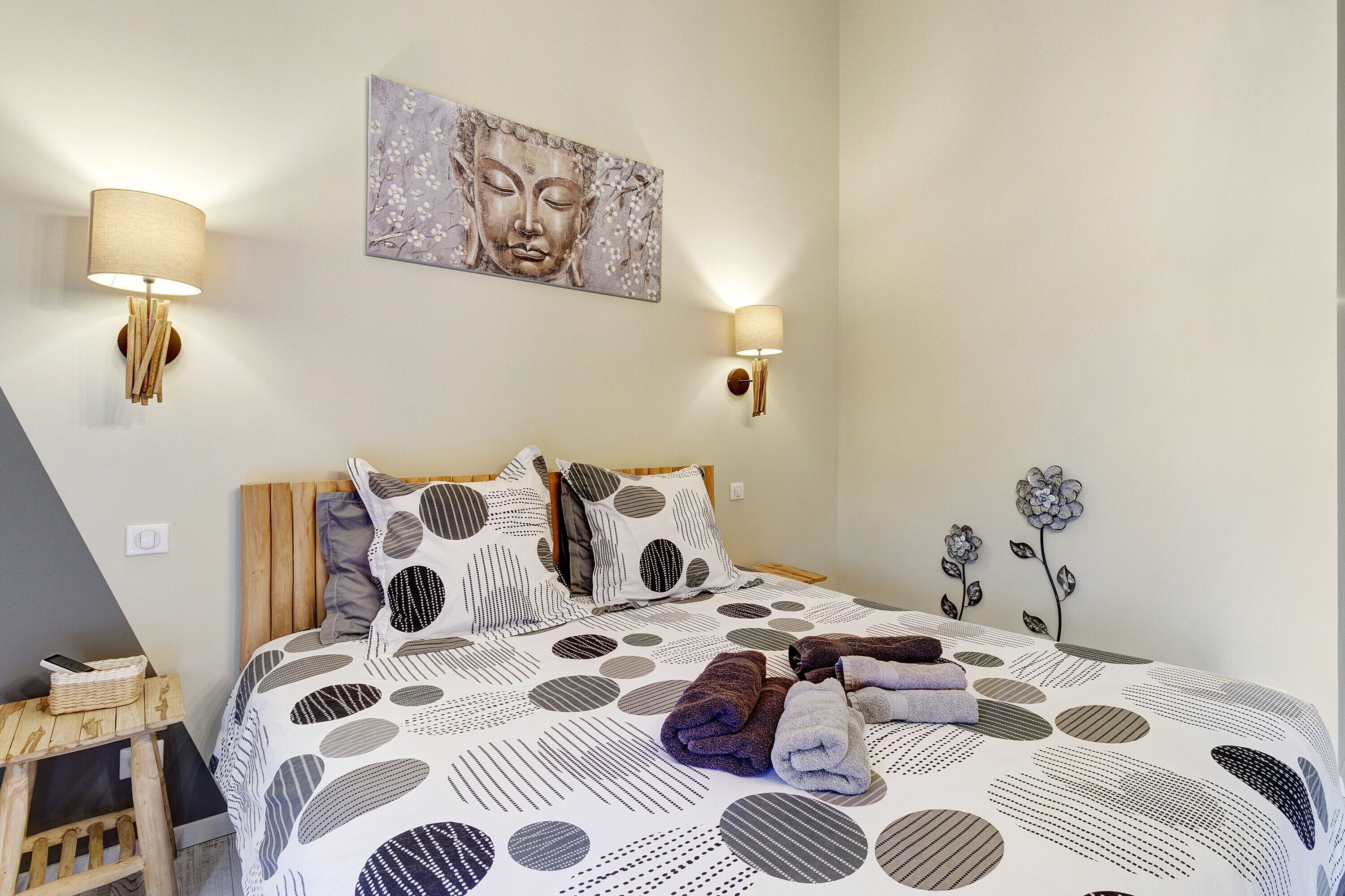 Une chambre à coucher avec un lit, des oreillers, une lampe fixée au mur, un tableau et un élément décoratif mural.