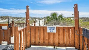 Una puerta de madera con un letrero que dice 'LAVAR PIES Y ARTÍCULOS AQUÍ' en la entrada de una playa.