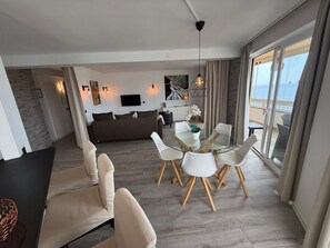 A modern living room with a glass dining table, white chairs, a sofa, and a TV mounted on the wall. - Exclusive Oceanfront Apartment in Fuengirola, Recently Renovated (Fuengirola)