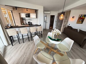 A modern kitchen with a central island, a dining area with a glass table and chairs, a sofa, and a decorative light fixture. - Exclusive Oceanfront Apartment in Fuengirola, Recently Renovated (Fuengirola)