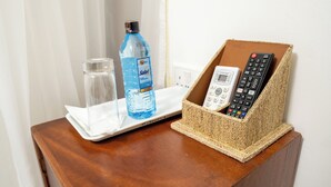 A wooden table with a glass of water, a bottle of water, and a remote control holder containing two remotes. - Whirlsprings Hotel Kisumu (Kisumu)