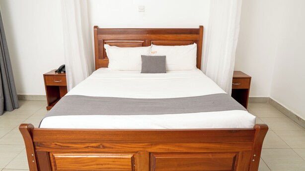 A neatly made bed with a wooden headboard, two bedside tables, and a telephone on one of the tables. - Whirlsprings Hotel Kisumu (Kisumu)