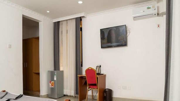Una habitación de hotel con una cama, un escritorio con una silla, un televisor, un refrigerador y un basurero.