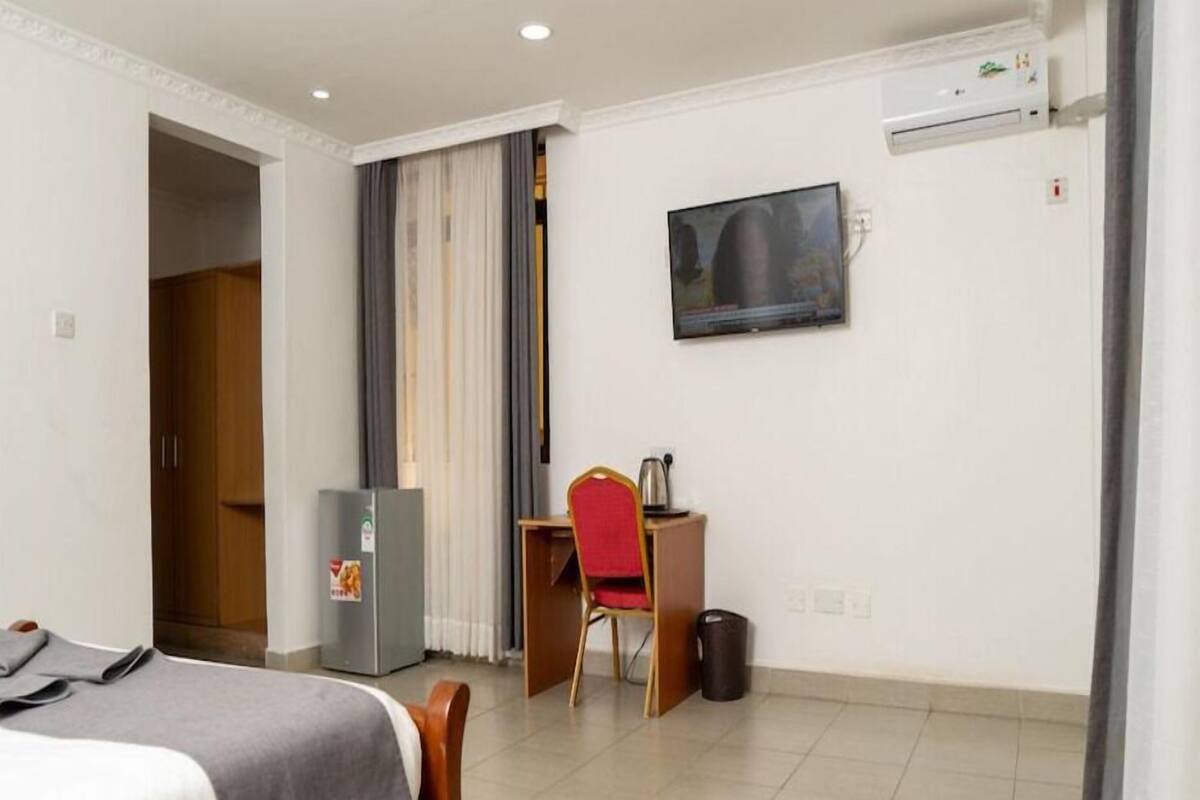 Una habitación de hotel con una cama, un escritorio con una silla, un televisor, un refrigerador y un basurero.