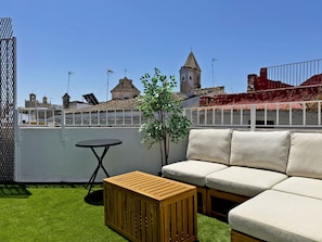 Eine Dachterrasse mit Holztisch, einer Couch und einer kleinen Pflanze.