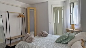 Une chambre à coucher comprenant un lit, un miroir, une armoire, un porte-vêtements et une fenêtre avec des rideaux.