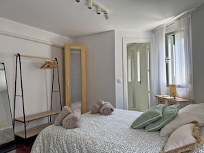 Ein Schlafzimmer mit einem Bett, einem Spiegel, einem Kleiderschrank, einer Kleiderstange und einem Fenster mit Vorhängen.