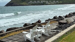 Vista costeira com costa rochosa, cadeiras brancas e calçada pavimentada.