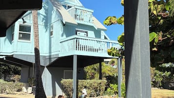 Een lichtblauw gebouw met een balkon, omgeven door groen en een heldere lucht.